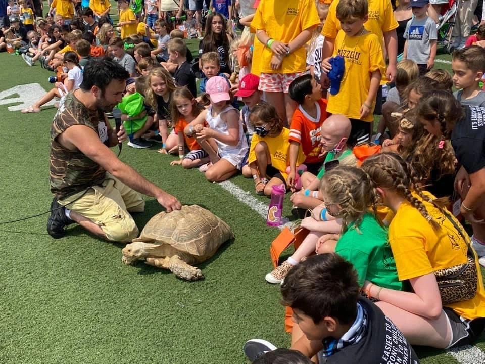A child holding a snake with a big smile at a birthday party show